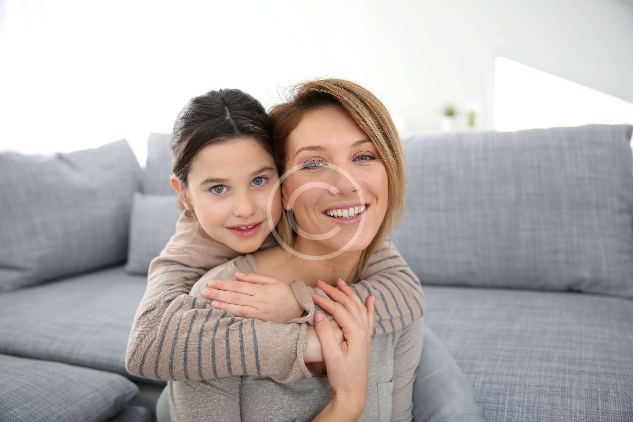 mamma e figlia si abbracciano e sorridono allegramente sedute sul divano