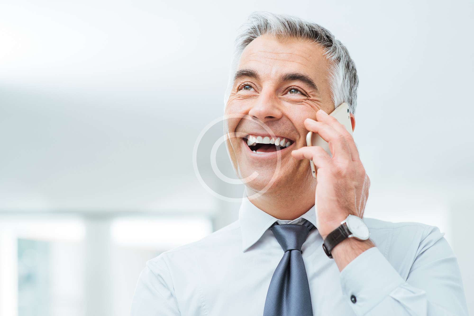 uomo brizzolato con camicia e cravatta sorride mentre con la mano sorregge il telefono all'orecchio